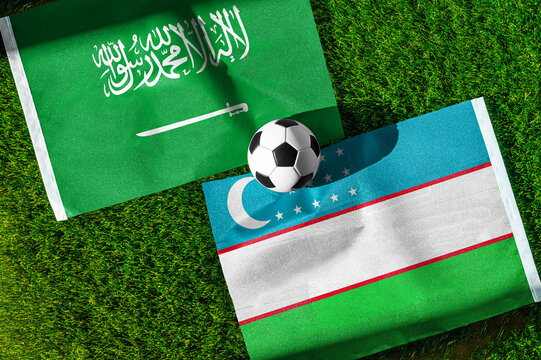 Saudi Arabia vs. Uzbekistan football match. National flags on green grass with soccer ball in the middle. Football background for international match.