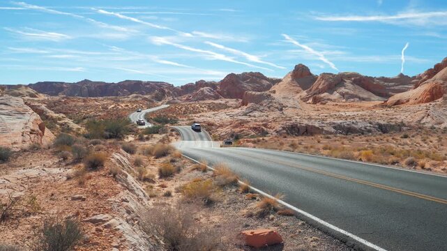 Scenic view of cars driving on winding road through hilly iconic red rock formations of valley of fire state park in nevada, showcasing beautiful desert landscape and a bright blue sky. Road trip