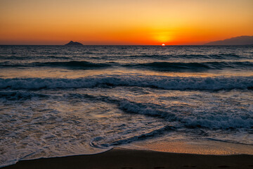 Fototapeta premium Sunset over the Libyan Sea at Kalamaki beach in Crete with orange sky, waves and distant island silhouettes