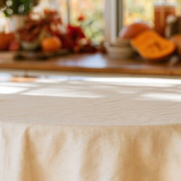Pale oat linen table surface with copy space, featuring a soft glowing farmhouse kitchen and autumn pumpkins for product mockups