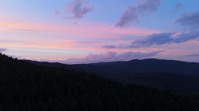 Aerial Orbit Flight Over Dark Forested Mountain Silhouette at Twilight With Pastel Sky