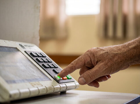 Elderly voter pressing confirmation button on electronic voting machine during democratic elections