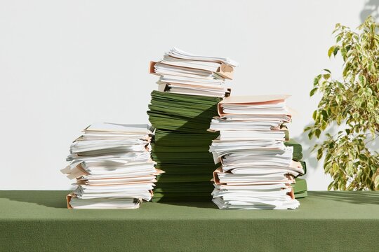 Tall stacks of folders and office papers creating a chaotic workload on a green desk, with a muted olive tone for administration and document management