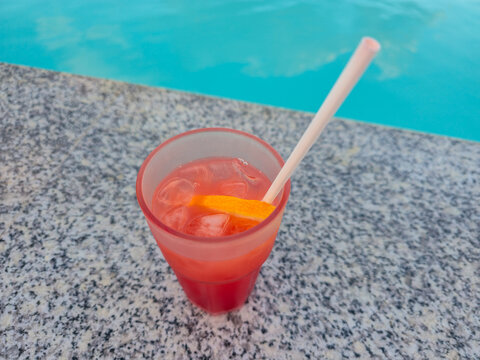 Cocktail glass by rooftop pool at sunset, red drink with straw on poolside ledge, tropical vacation relaxation concept for tourism and leisure