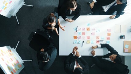Obraz premium Top view of investor writing white board to present project and putting hand together with professional business team to celebrate successful project at meeting table with sticky note. Directorate.