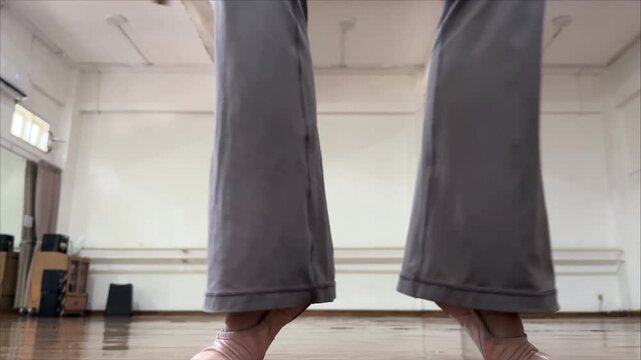 Footage of Low angle close up of an adult female ballet dancer feet performing alternating heel raises onto demi-pointe in soft ballet shoes. showing footwork, and  ankle strengthening dance practice.