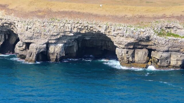 Tracking telephoto aerial shot of a cave and cliffs on the Jurassic coastline near Dancing Ledge, Dorset, UK