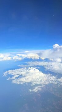 Aerial view of fluffy white clouds over a vast blue ocean and distant landmass under a clear sky during daytime. Slow motion vertical footage, 4K, copyspace