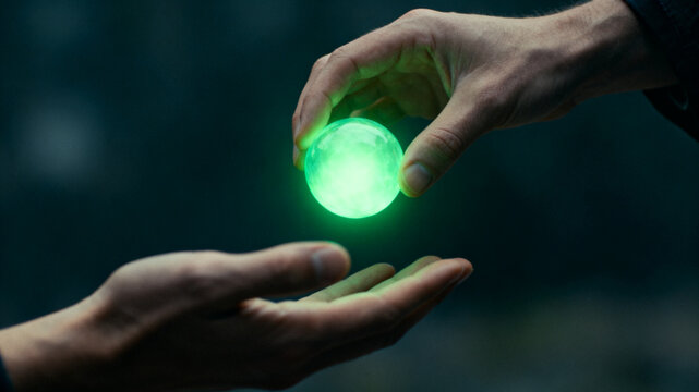 Human hand passing a glowing green light orb to another hand, symbolizing energy transition, dark moody background