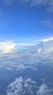 Aerial view of fluffy white clouds against a bright blue sky with soft gradients and sunlight illuminating the scene from above. Slow motion vertical footage, 4K, copyspace