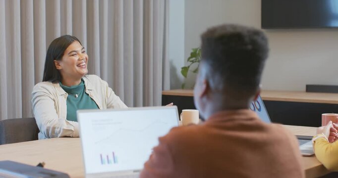 African adult woman laughing, leaning back at conference table after colleague showing charts