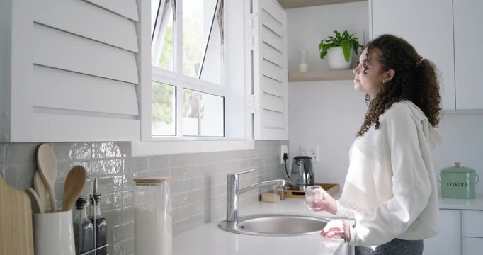 Thirst driving teen in hoodie at kitchen sink filling glass sipping gazing leaving glass