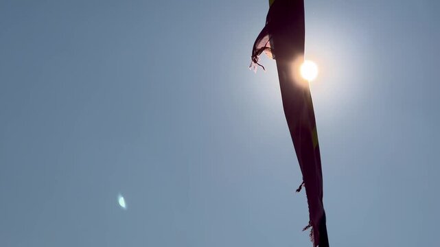 Sunlight shines through a tattered flag waving against a clear blue sky