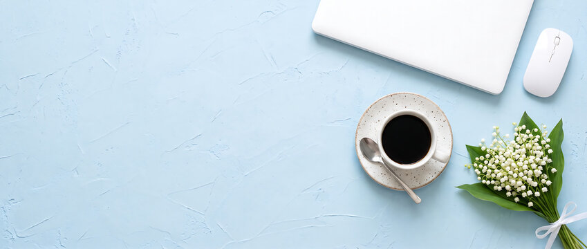 Laptop computer with coffee cup and flowers on a light blue textured background with copy space