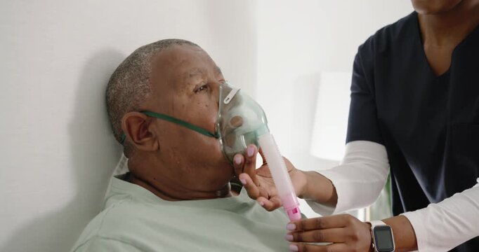 African American nurse in scrubs fitting oxygen mask spacer tubing on man needing O2 bedside