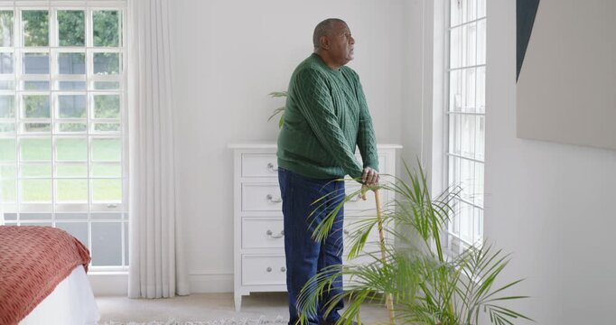 African American man in green sweater bracing cane, gazing out grid window as camera nears