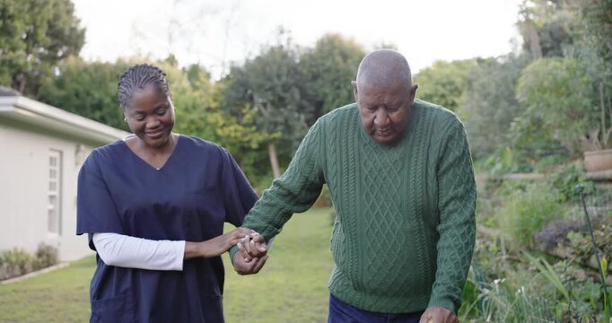 African American caregiver offering arm, steadying senior man walking in garden with cane, scrubs