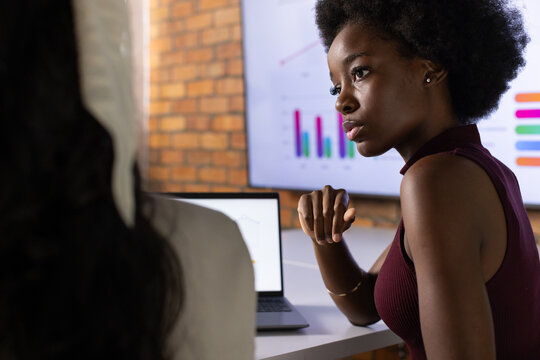 Female coworkers reviewing charts at office, woman in burgundy top pointing at laptop, copy space