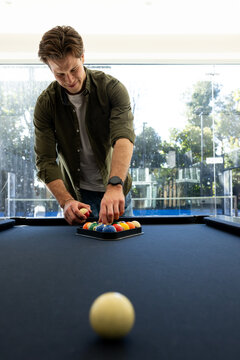 Man leaning over black-felt pool table placing colorful billiard balls into triangle rack