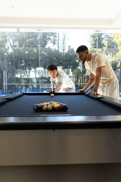 Male friends playing pool on blue-felt table in game room, wearing casual shirts, rack of balls