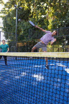 Two male players leaping, swinging black paddles on blue court with net, light purple shirt