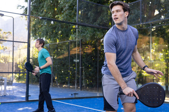 Two men playing padel on blue court wearing gray-blue shirt and light gray shorts, holding rackets
