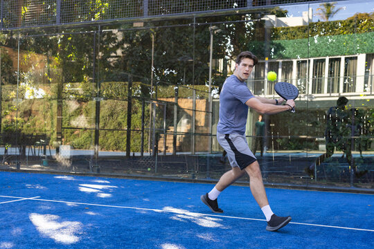 Adult male lunging on blue paddle court, holding paddle, gray shirt, eyeing yellow ball, copy space