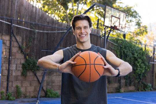 Man standing on blue backyard court holding orange basketball with portable hoop and wearing watch