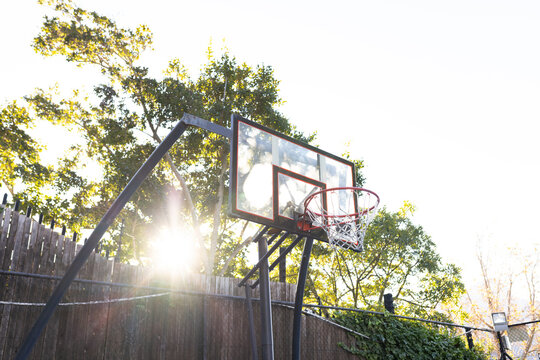 Basketball hoop with clear backboard is standing on black pole near wooden fence, rim and net
