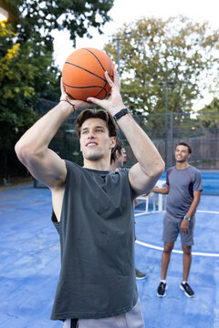 Male friends watching shooter in dark tank holding orange basketball, preparing shot on blue court