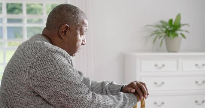 Senior African American man sitting on bed holding cane, window light drawing gaze