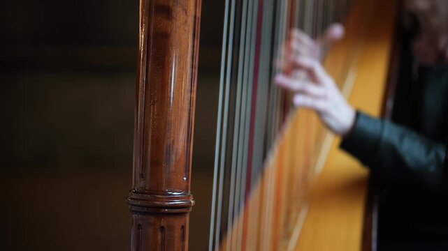 Close-up of hands playing a classical harp with wooden frame
