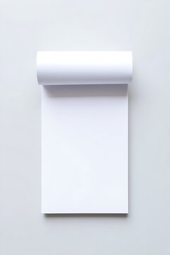 Blank white paper notepad pad with rolled top resting on neutral grey surface