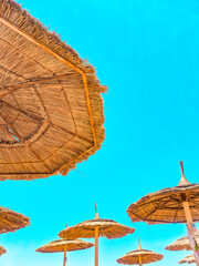 straw beach umbrellas under bright blue sky © Laura