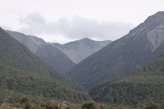 mountainous alpine landscape, steep forested slopes rising to rocky peak (wide-angle, panorama, overcast-sky, moving-train-view) 6712