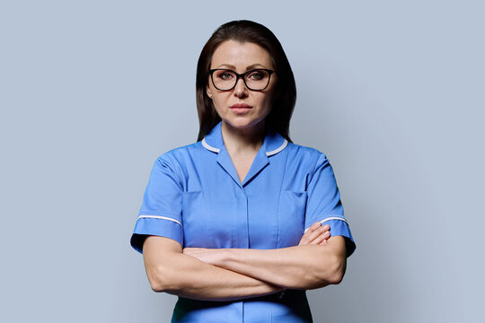 Mature female doctor or nurse with crossed arms on grey background