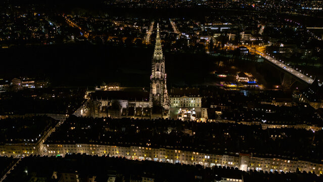 Drone aerial night view of Bern Minster cathedral tower and Old Town illuminated in winter, Switzerland