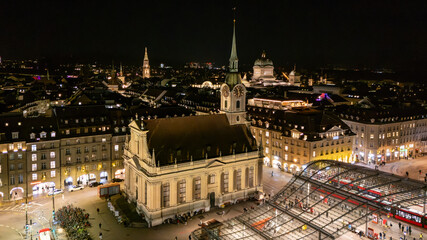 Aerial drone view of Heiliggeistkirche church and Bahnhofplatz glass canopy illuminated at night in Bern, Switzerland © Cirrus Height