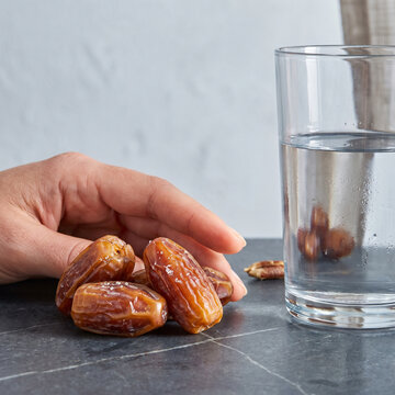 Hand reaching for dates next to a glass of water on a table  