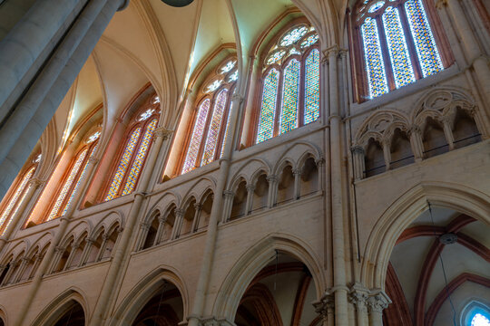 Interior view of a grand Gothic cathedral with a rose window and rows of wooden pews. Lyon