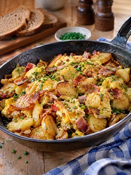 Herzhaftes Bauernfr&uuml;hst&uuml;ck aus knusprigen Bratkartoffeln, Ei, Speck, Zwiebeln und Schnittlauch in der Pfanne &ndash; deftige deutsche Hausmannskost, frisch zubereitet.