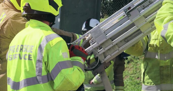 Firefighter crew &ndash; emergency service fireman rescue in action. In uniform in response to fire with firefighting ladder loading on fire engine truck.