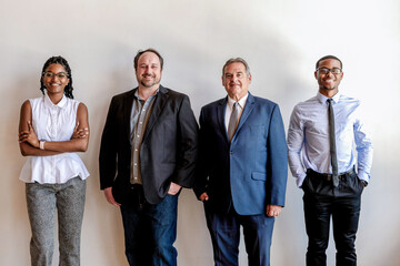 Obraz premium Four professionals standing against a white wall, smiling confidently.