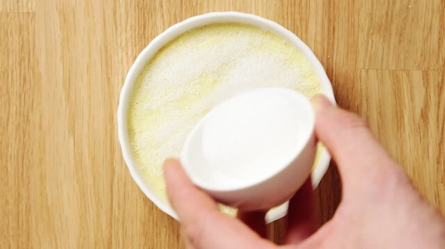 Sugar is sprinkled over crema catalana in ramekin. Homemade Spanish dessert waits for torch before dinner party serving. Crisp caramel top makes sweet finish for family meal, holiday table or guests.