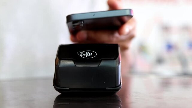 Person paying with smartphone using nfc technology for contactless mobile payment on a pos terminal at a store counter