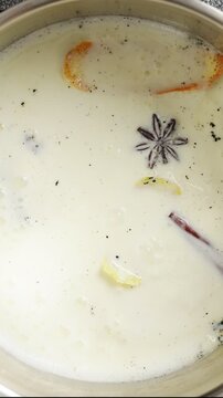 Milk bubbles with citrus zest, cinnamon and vanilla in saucepan. Pastry school lesson shows gentle heat for extracting flavour. Infused milk makes custard for crema catalana, pudding or pastry cream.