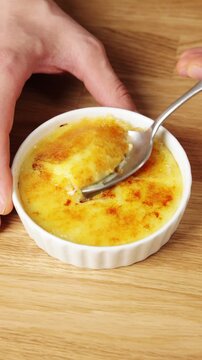 Spoon breaks crisp sugar crust and lifts crema catalana. Custard looks thick and smooth under caramel topping. Cold Spanish dessert has sweet vanilla, fresh citrus flavour and creamy center.