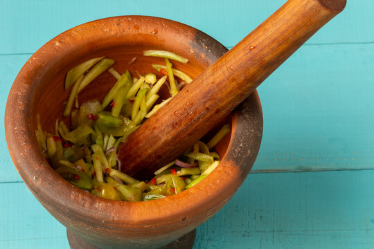 Thai Som Tam-style salad made with unripe Charentais melon in a clay mortar with a wooden pestle, on blue-painted boards.