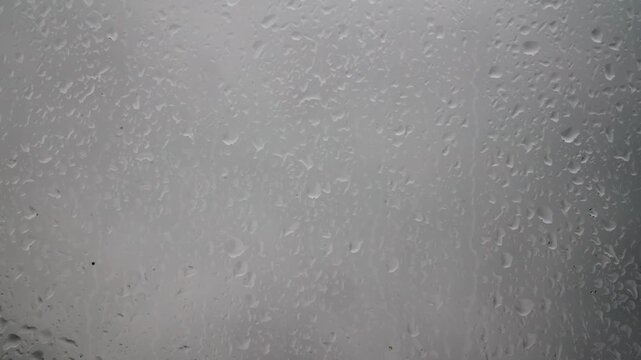 Raindrops on window glass texture with an overcast gray background perfect for overlays