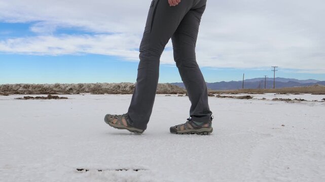Close up view of unrecognizable person legs and feet wearing hiking pants and sandals while walking across white salt crystals in death valley national park